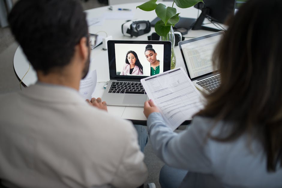 Two professionals conduct a virtual job interview using laptops in a modern office